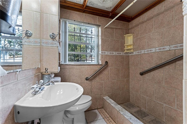 bathroom featuring tiled shower, toilet, sink, and tile walls