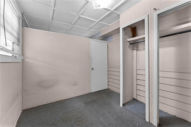 unfurnished bedroom with wooden walls, dark carpet, and two closets