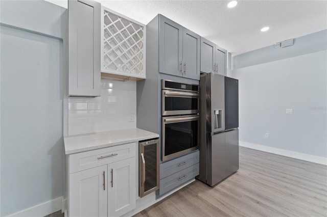 kitchen with wine cooler, backsplash, stainless steel appliances, light stone countertops, and light hardwood / wood-style flooring