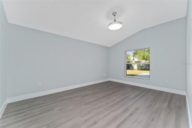 empty room featuring light hardwood / wood-style flooring, vaulted ceiling, and a textured ceiling