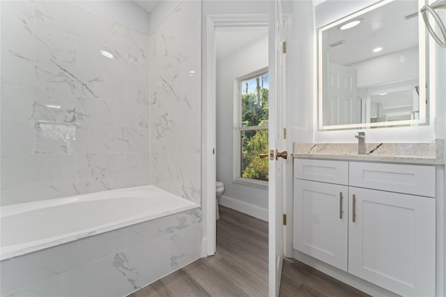 full bathroom with vanity, hardwood / wood-style floors, tiled shower / bath combo, and toilet