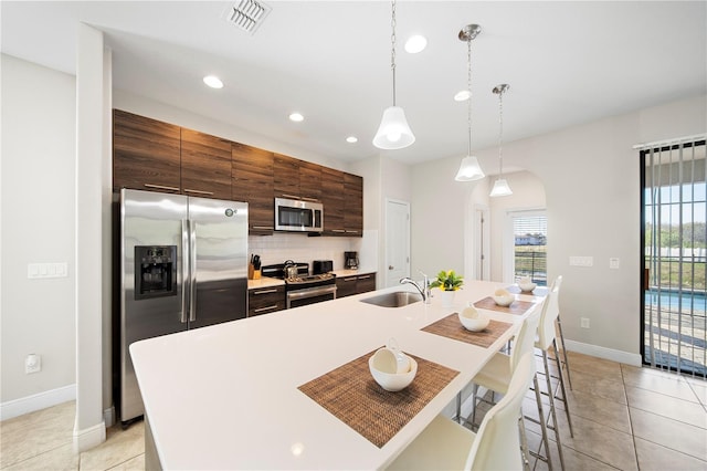 kitchen featuring sink, decorative light fixtures, appliances with stainless steel finishes, an island with sink, and decorative backsplash