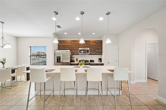 kitchen featuring stainless steel appliances, hanging light fixtures, a center island with sink, and a kitchen breakfast bar