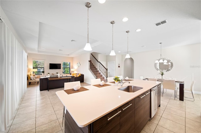 kitchen featuring dark brown cabinetry, sink, light tile patterned flooring, and a center island with sink