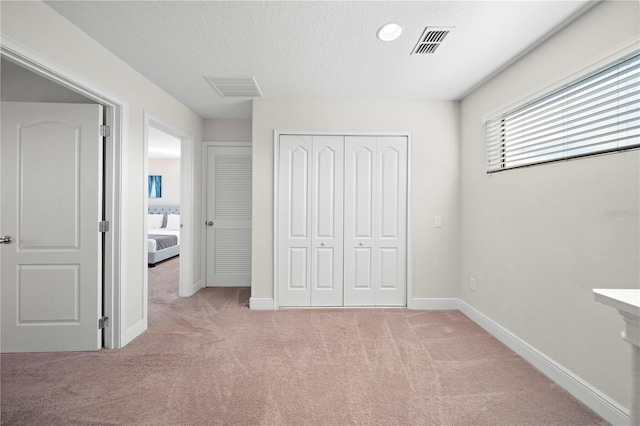 unfurnished bedroom with light colored carpet, a textured ceiling, and a closet