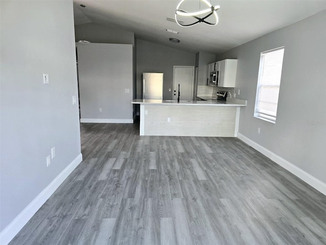 kitchen with white cabinetry, tasteful backsplash, wood-type flooring, vaulted ceiling, and kitchen peninsula