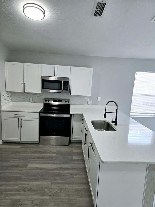 kitchen with appliances with stainless steel finishes, white cabinetry, sink, kitchen peninsula, and dark wood-type flooring