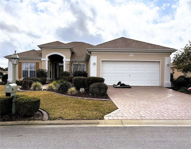 view of front of property with roof with shingles, an attached garage, decorative driveway, a front lawn, and stucco siding