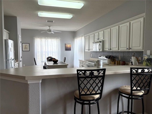 kitchen with a breakfast bar area, light countertops, ceiling fan, white appliances, and a peninsula