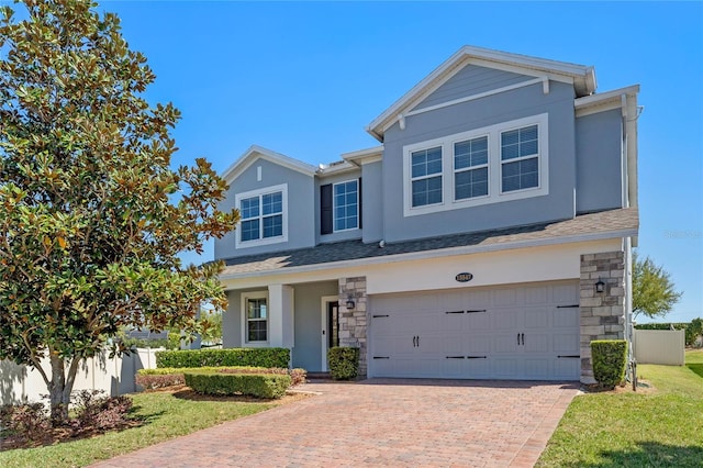 view of front of house featuring stucco siding, decorative driveway, stone siding, fence, and a garage