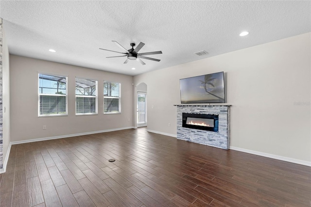 unfurnished living room with a wealth of natural light, visible vents, dark wood-type flooring, and a glass covered fireplace