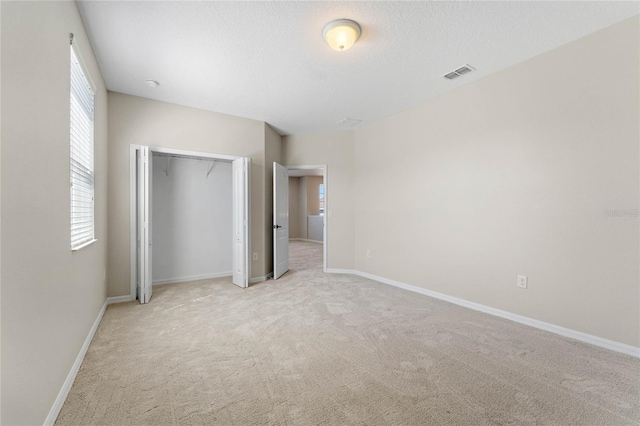 unfurnished bedroom with visible vents, baseboards, a closet, a textured ceiling, and light colored carpet