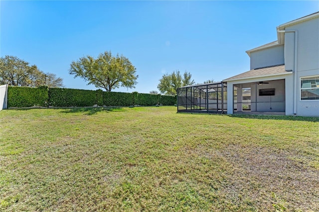 view of yard featuring glass enclosure, fence, and a ceiling fan