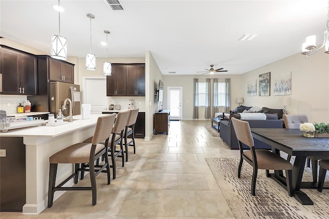 kitchen featuring a kitchen island with sink, hanging light fixtures, dark brown cabinets, stainless steel refrigerator with ice dispenser, and a kitchen bar