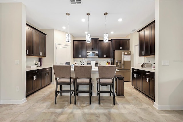 kitchen featuring a kitchen island with sink, hanging light fixtures, dark brown cabinets, and stainless steel appliances