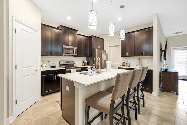 kitchen featuring sink, a breakfast bar, stainless steel appliances, a center island with sink, and decorative light fixtures