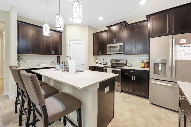 kitchen featuring dark brown cabinetry, sink, a center island with sink, appliances with stainless steel finishes, and pendant lighting