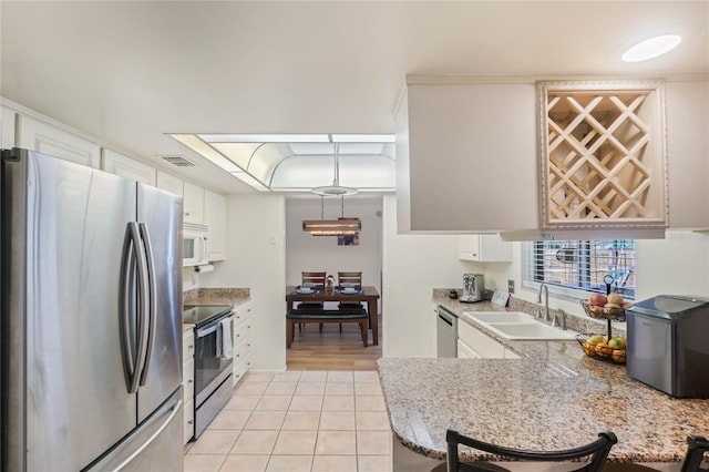 kitchen with light tile patterned flooring, sink, kitchen peninsula, stainless steel appliances, and white cabinets