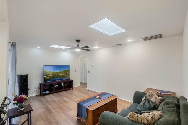 living room featuring ceiling fan, a skylight, and light wood-type flooring