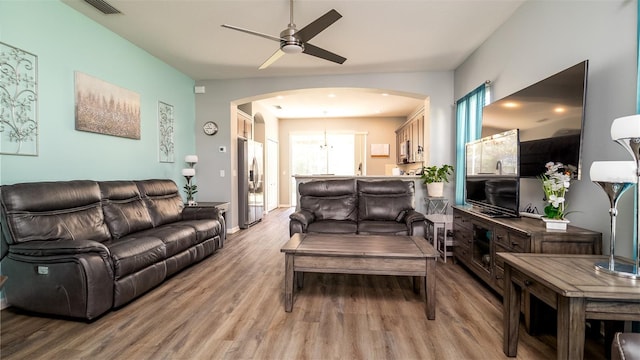 living room featuring arched walkways, visible vents, ceiling fan, and light wood finished floors