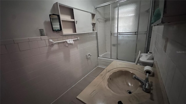 full bathroom featuring tile walls, sink, toilet, and combined bath / shower with glass door