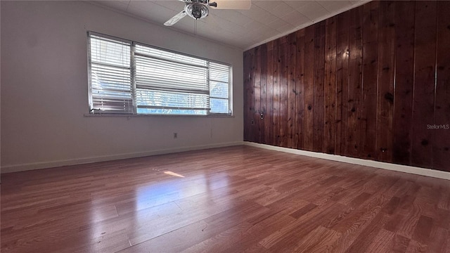 unfurnished room with crown molding, ceiling fan, wooden walls, and hardwood / wood-style floors