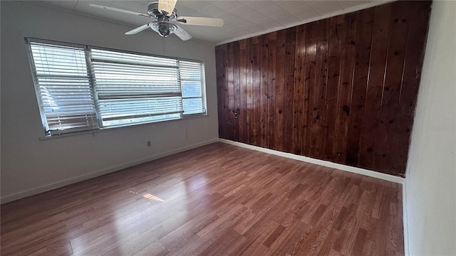 unfurnished room featuring ceiling fan, wood-type flooring, and wooden walls