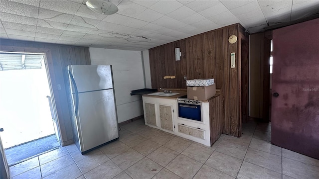 kitchen with fridge, light tile patterned floors, sink, and wood walls