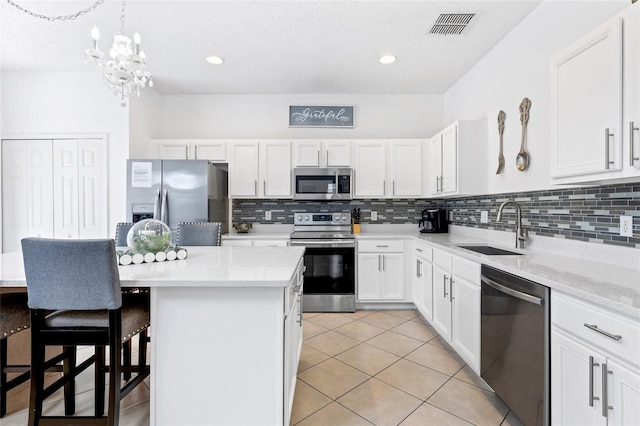 kitchen with a kitchen island, appliances with stainless steel finishes, sink, white cabinets, and hanging light fixtures