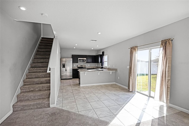 kitchen with light tile patterned floors, a breakfast bar area, stainless steel appliances, and kitchen peninsula