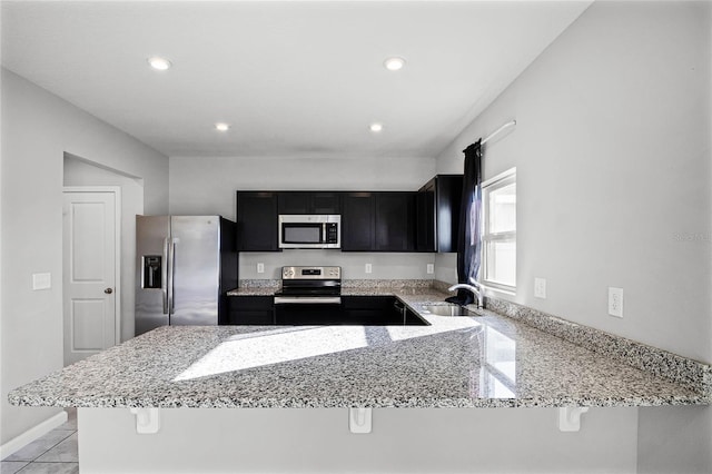 kitchen featuring light stone counters, stainless steel appliances, kitchen peninsula, and sink