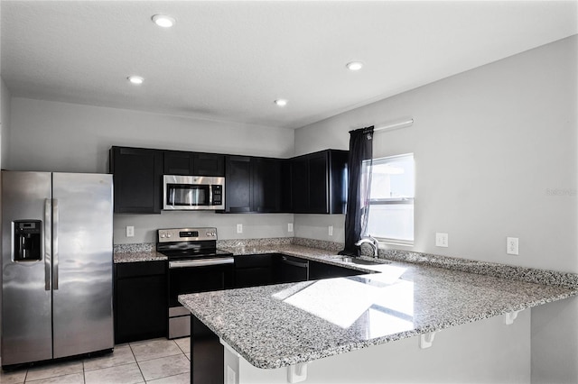 kitchen featuring a breakfast bar, sink, kitchen peninsula, stainless steel appliances, and light stone countertops