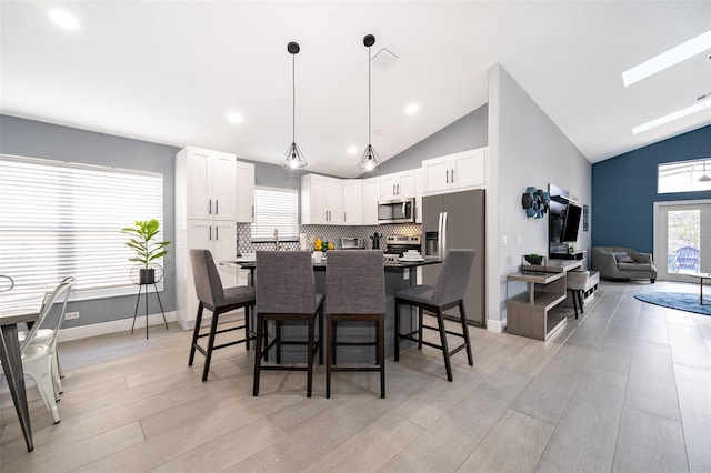 dining space featuring a skylight, high vaulted ceiling, and light hardwood / wood-style flooring