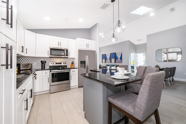 kitchen with appliances with stainless steel finishes, hanging light fixtures, a breakfast bar area, and white cabinets