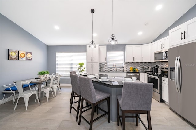 kitchen featuring stainless steel appliances, white cabinetry, lofted ceiling, and decorative light fixtures