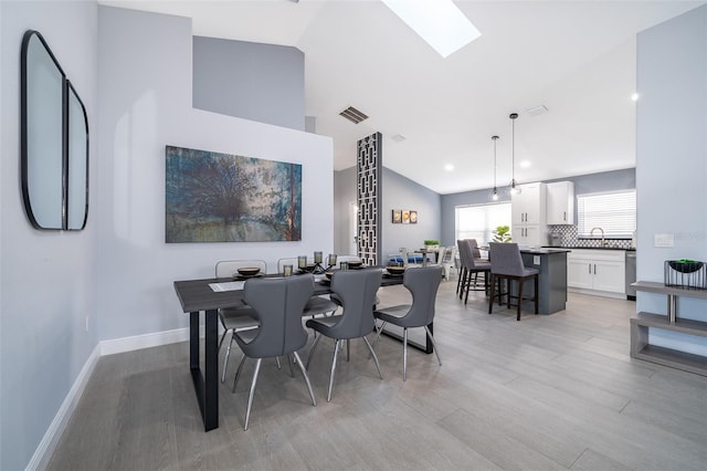 dining space with a skylight, high vaulted ceiling, and light wood-type flooring