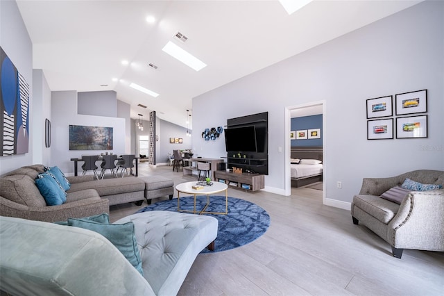 living room with a skylight, high vaulted ceiling, and light wood-type flooring