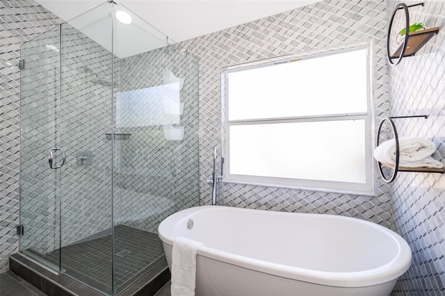 bathroom featuring shower with separate bathtub and tile walls