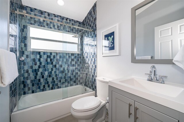 full bathroom featuring vanity, combined bath / shower with glass door, and toilet