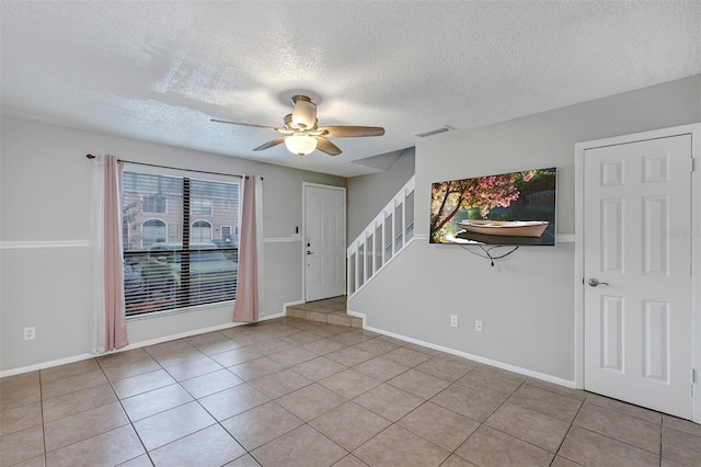 empty room featuring visible vents, baseboards, ceiling fan, stairway, and tile patterned floors