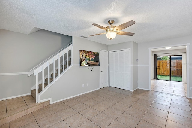 unfurnished room with visible vents, stairway, a ceiling fan, light tile patterned flooring, and baseboards