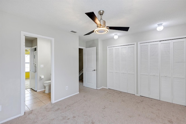 unfurnished bedroom featuring visible vents, tile patterned flooring, a textured ceiling, carpet flooring, and multiple closets