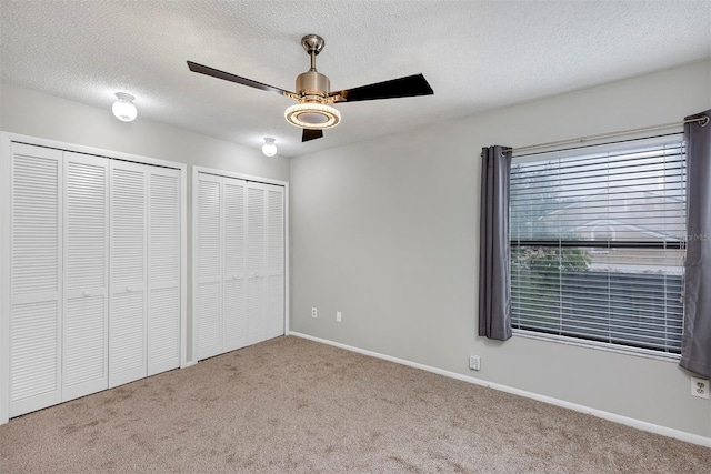 unfurnished bedroom with carpet, multiple closets, ceiling fan, a textured ceiling, and baseboards