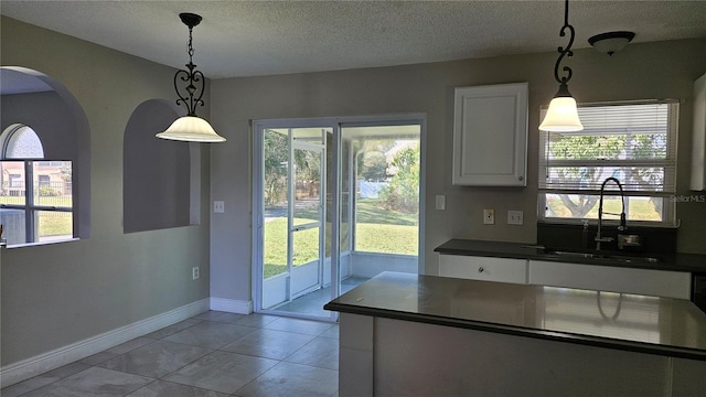 kitchen featuring sink, white cabinets, hanging light fixtures, light tile patterned floors, and a textured ceiling