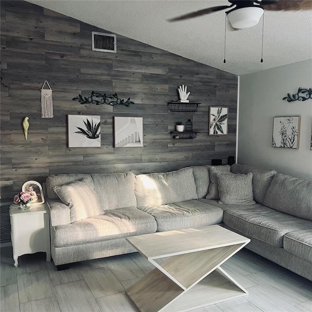 living room featuring lofted ceiling, a textured ceiling, ceiling fan, and wood walls