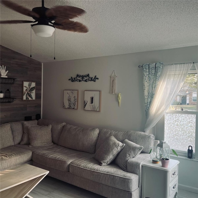 living room featuring ceiling fan, wood-type flooring, a textured ceiling, and wood walls