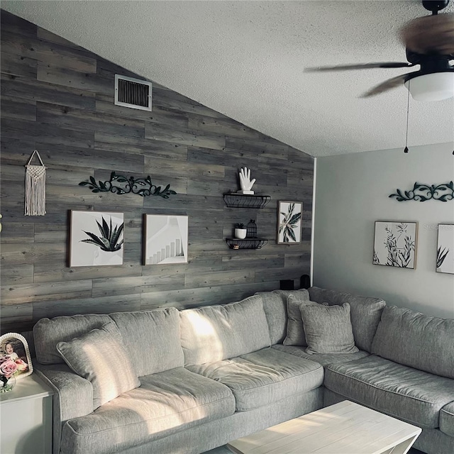 living room featuring lofted ceiling, wooden walls, a textured ceiling, and ceiling fan