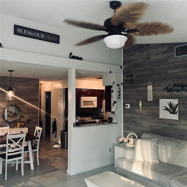 living room with ceiling fan, wooden walls, and a textured ceiling