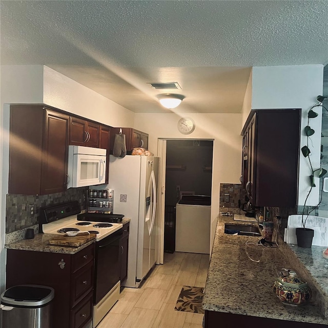 kitchen with sink, white appliances, dark brown cabinetry, washer / clothes dryer, and dark stone counters