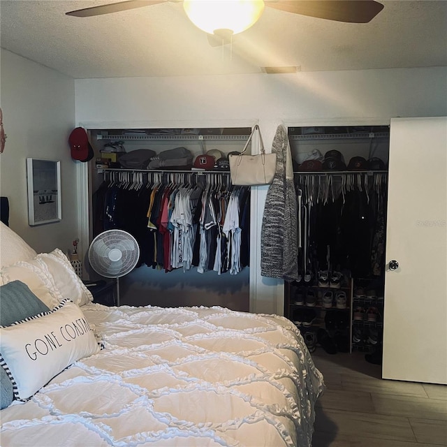 bedroom with ceiling fan, hardwood / wood-style floors, a textured ceiling, and two closets